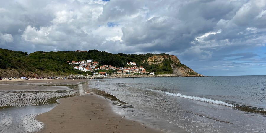 A beach with houses nestled under a cliff and a headland stretching out to sea.