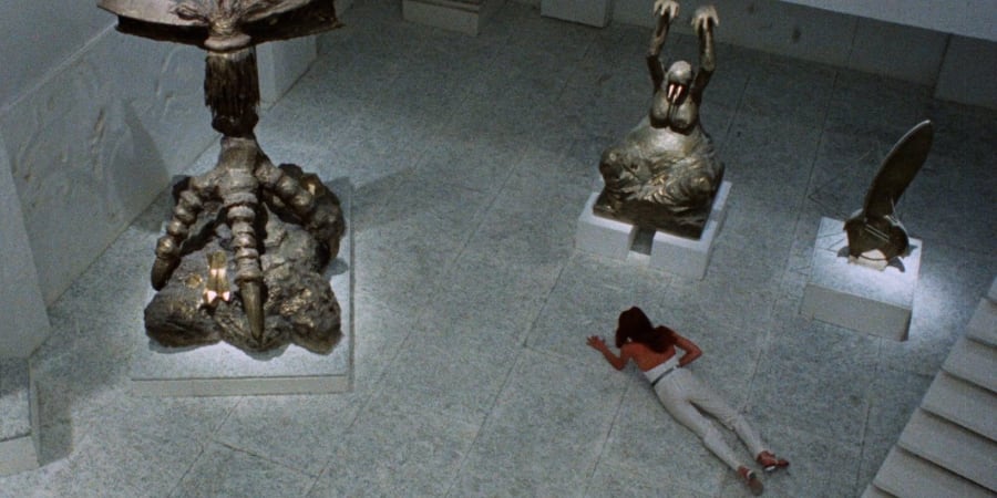 A woman lies on the floor of an art gallery with creepy sculptures looming over her